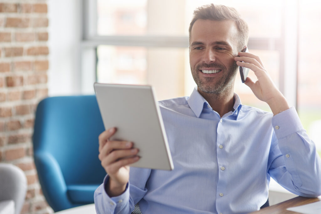 Man sat at his desk smiling whilst on the phone looking at his notes